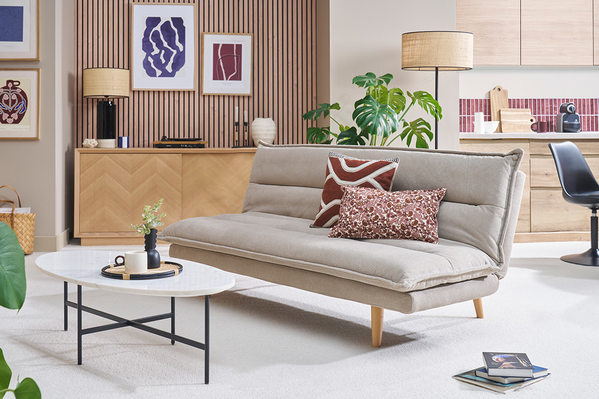 Canap� convertible beige en tissu chenille avec pieds en bois, vue de c�t� dans un salon moderne.
