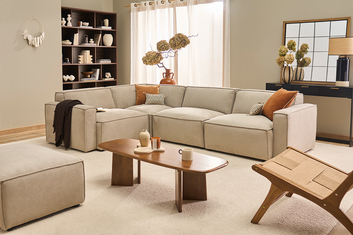 Canap� d'angle modulable en tissu beige dans un salon �l�gant, avec table en bois et objets d�coratifs.