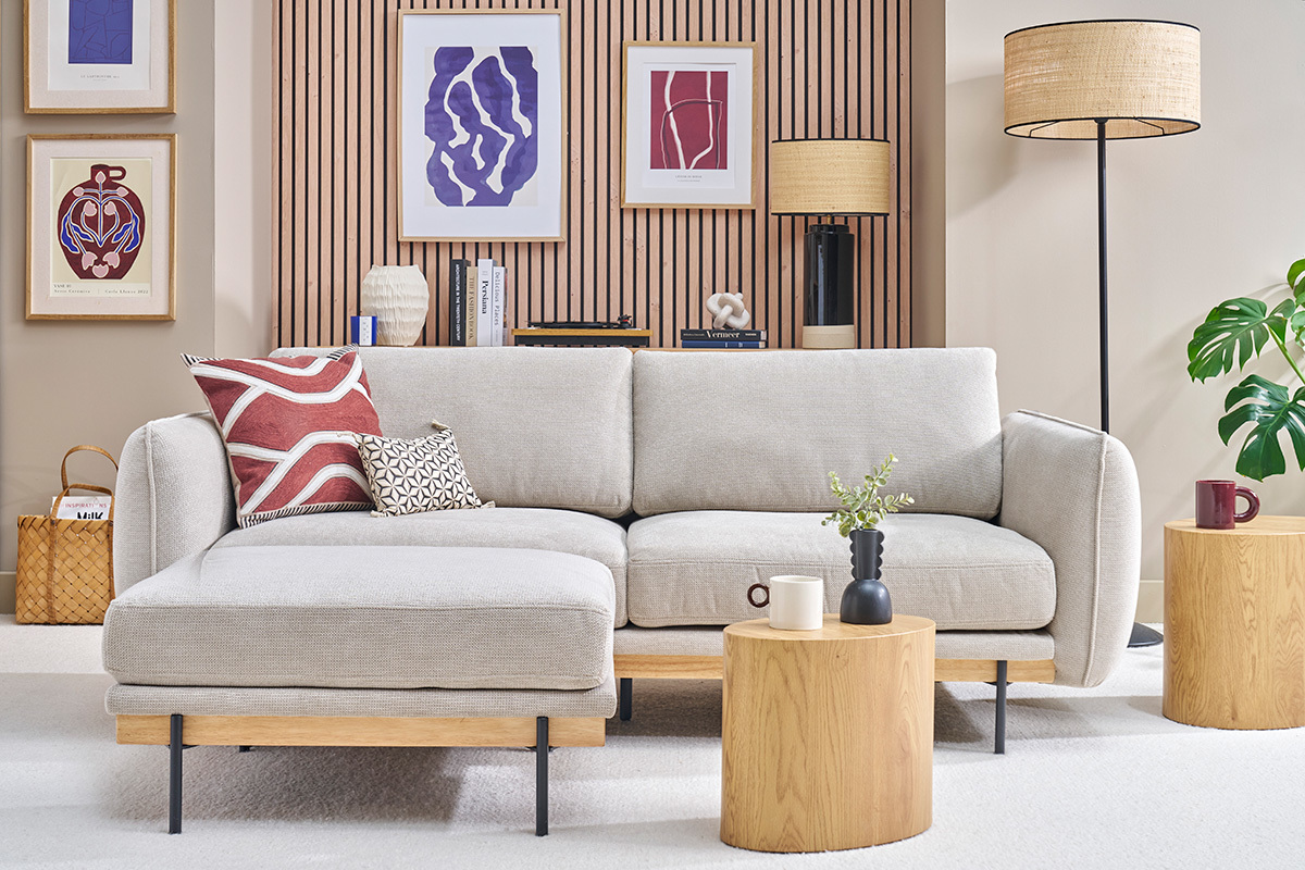 Canap� beige 3 places avec repose-pieds, angle frontal, entour� de tables en bois et d�cor mural moderne.