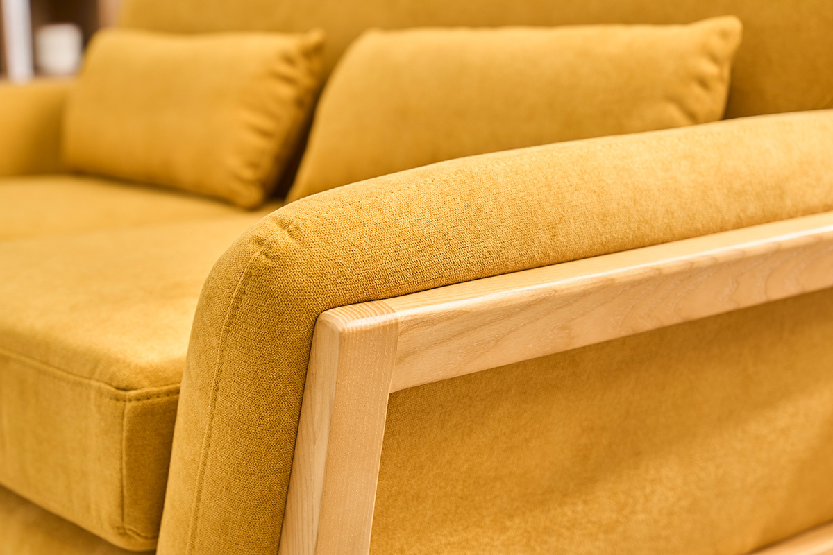 D�tail d'un canap� scandinave 2 places en tissu jaune moutarde avec accoudoir en bois clair.