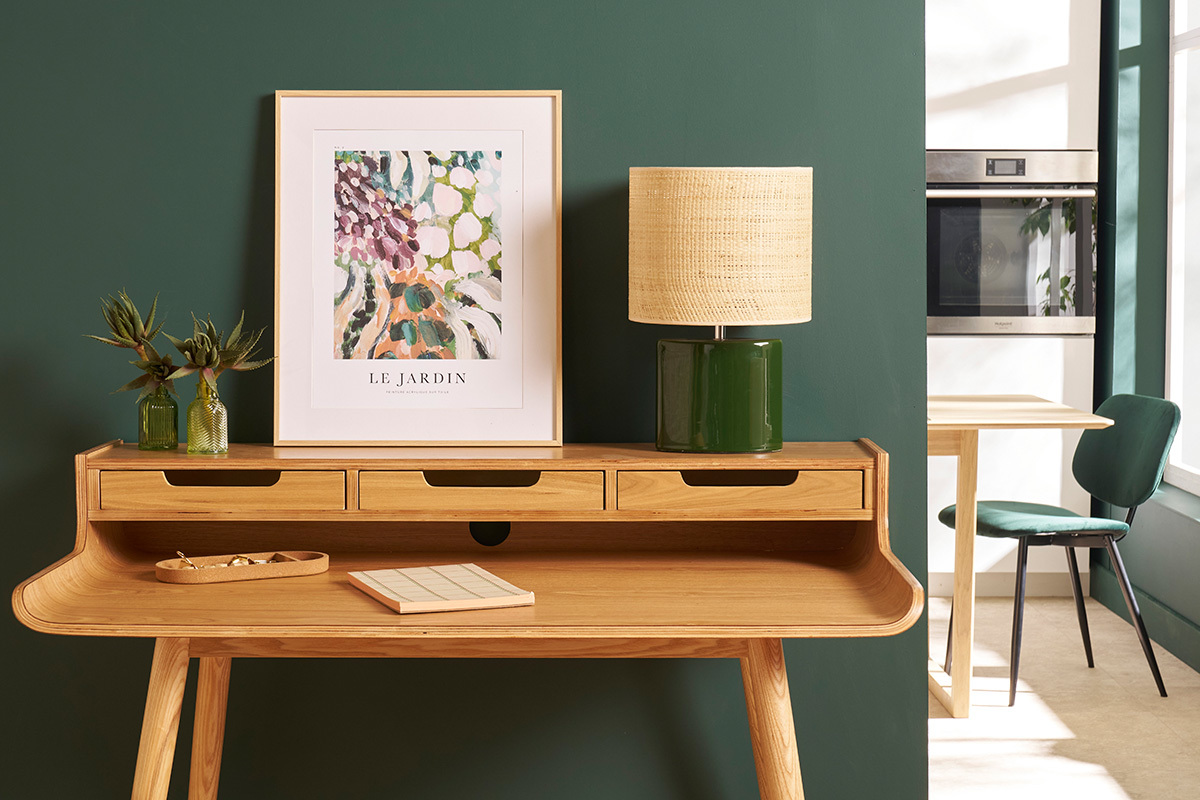 Lampe � poser TIGA en c�ramique vert fonc� avec abat-jour en raphia, sur une table en bois.