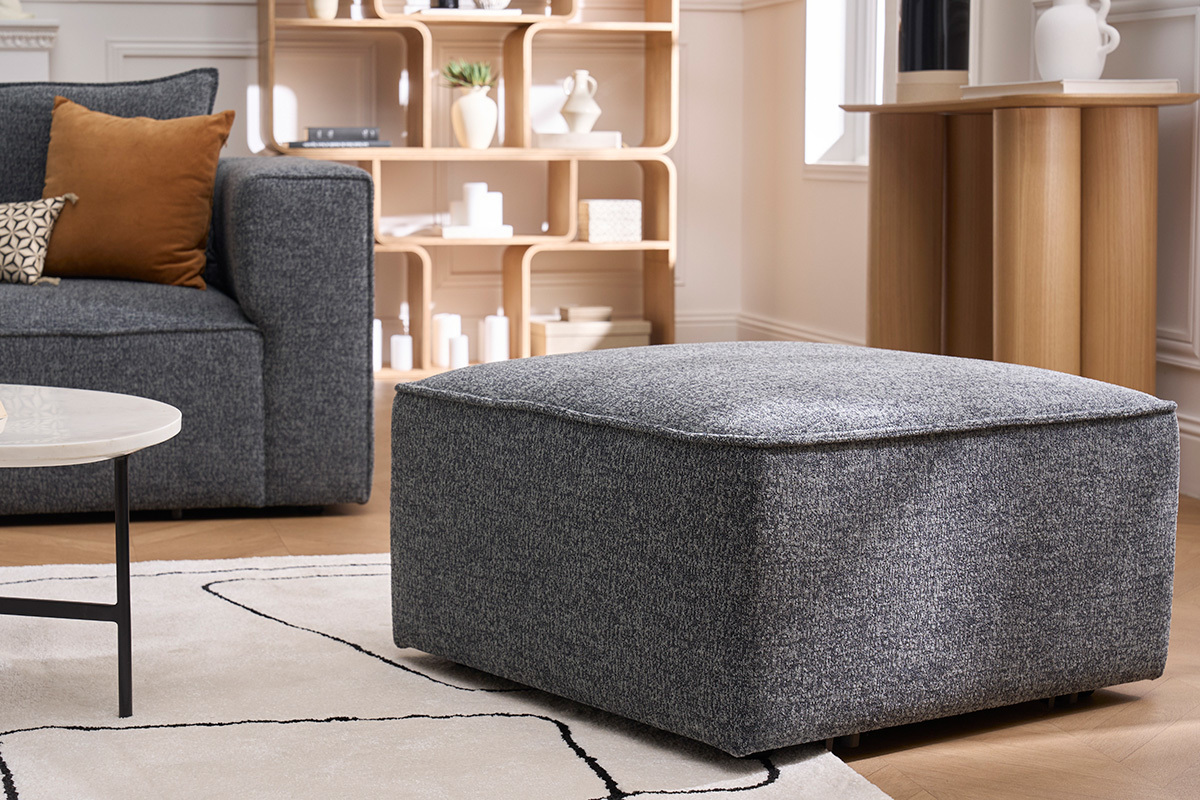 Pouf repose-pieds en tissu gris KERRY, vue en 3/4 dans un salon moderne.