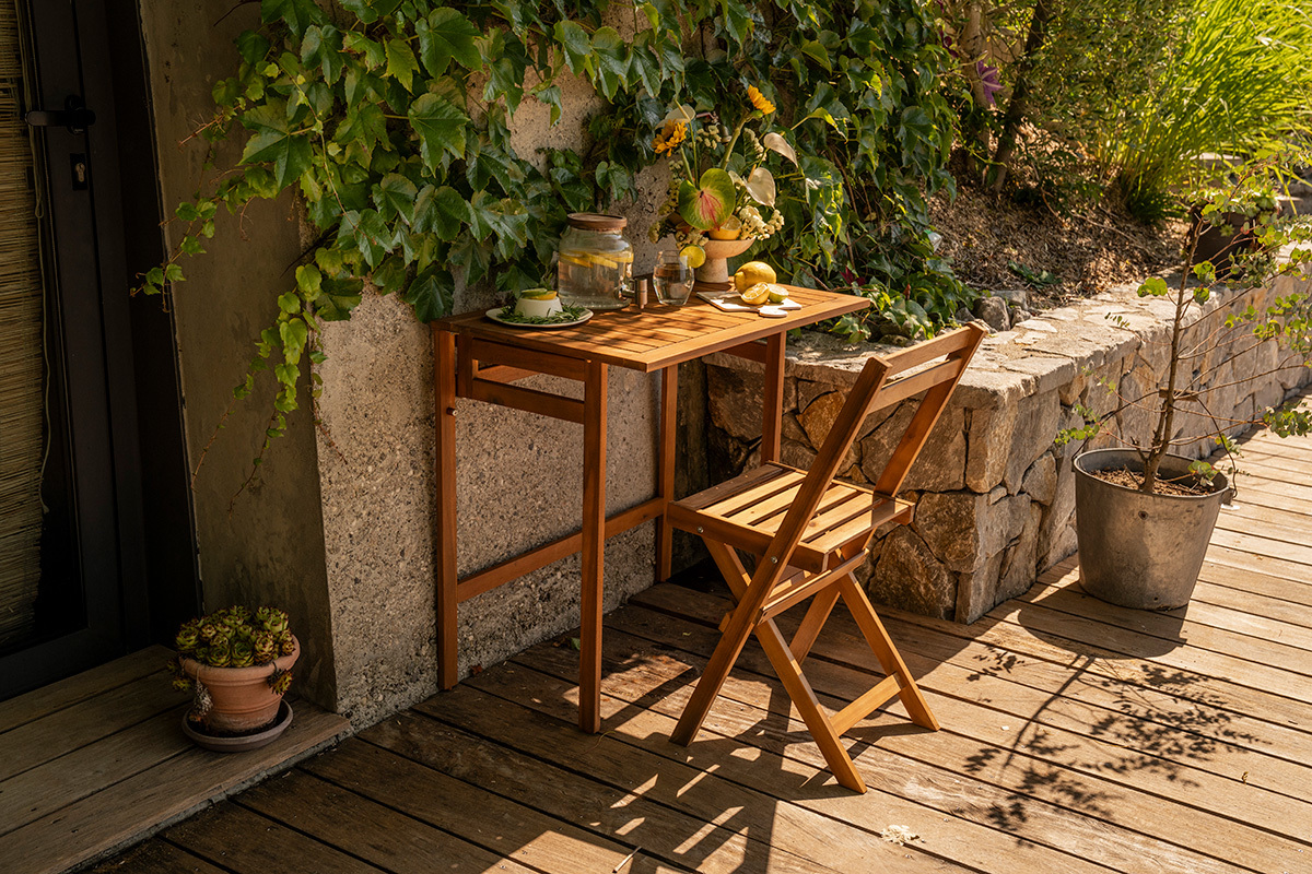 Table de balcon pliante en bois massif L80 cm, vue de 3/4 avec chaise et d�corations sur un balcon