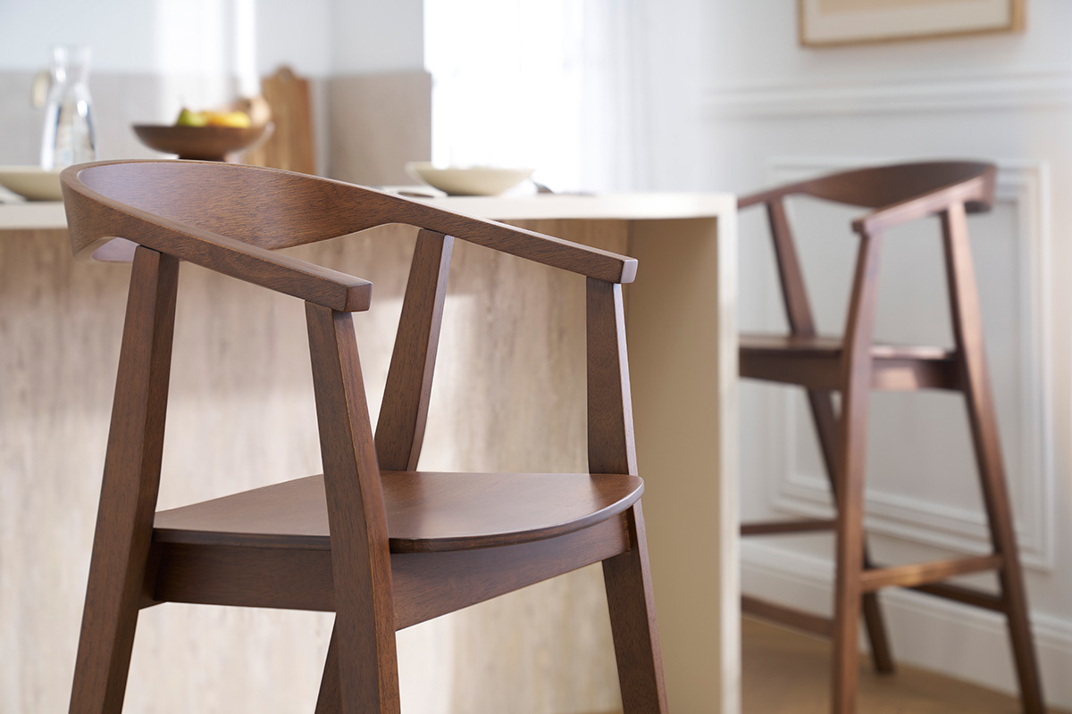 Deux tabourets de bar scandinaves en bois fonc� vue de c�t� pr�s d'un �lot de cuisine.